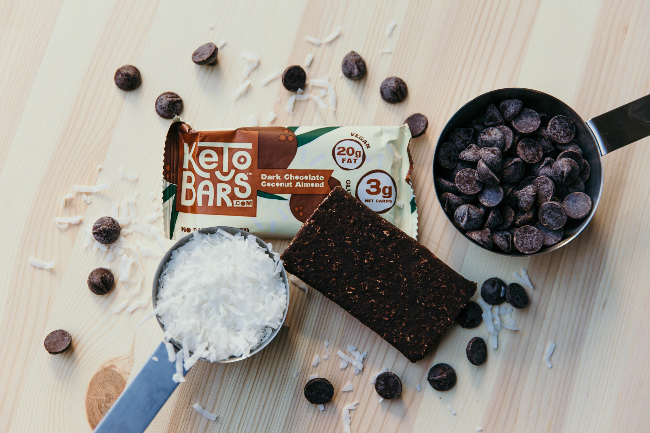 A Keto Bar next to a cup of chocolate chips and shredded coconut