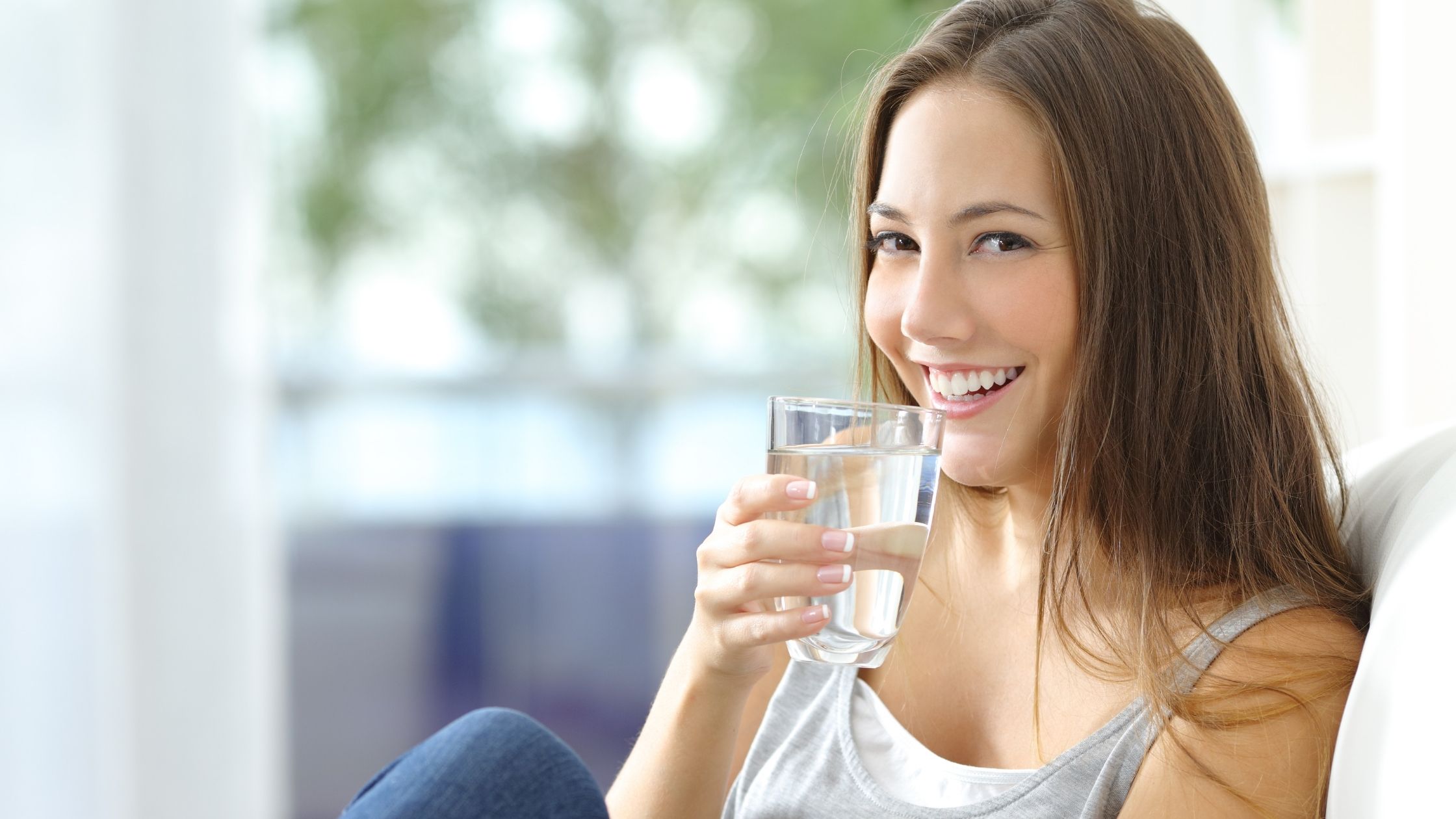 A young girl sitting on the couch enjoying a filtered glass of pure water