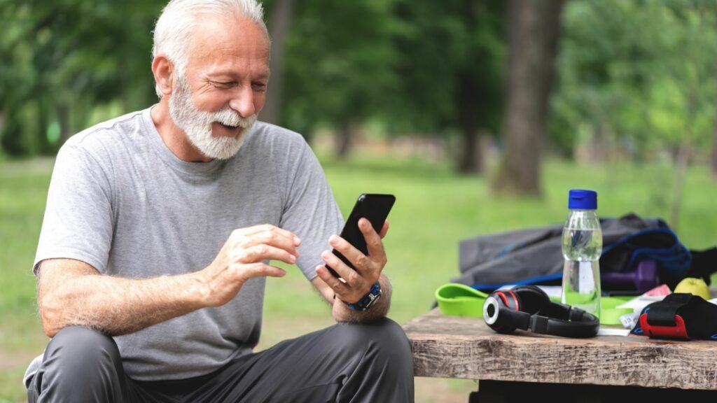 A bearded man sitting on a park bench logging his water intake into an app on his phone