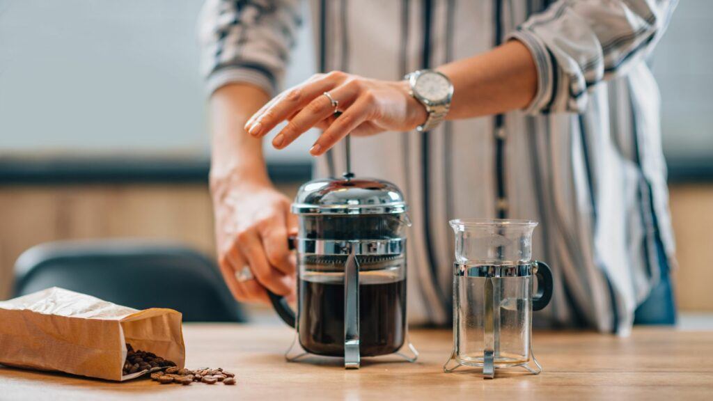 A person using a French press to prepare their dairy-free bulletproof coffee