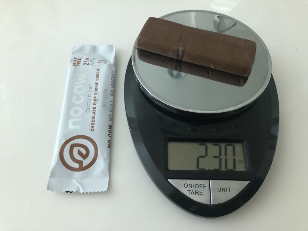 A No Cow Protein Bar on a food scale that reads 2.3oz