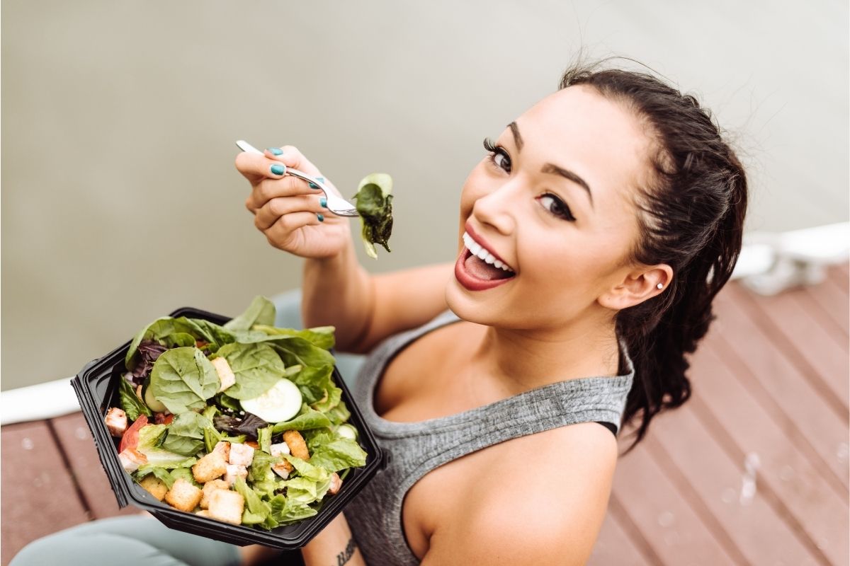 A beautiful women wearing active wear and eating a vegan keto salad